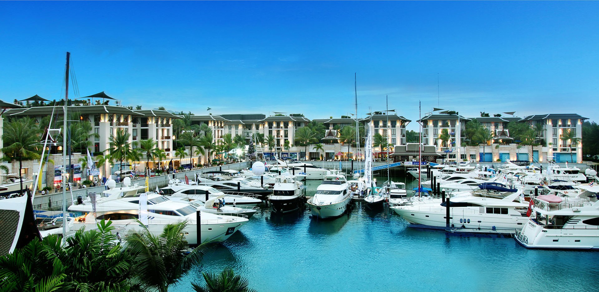 Motor yachts and sailing boats moored at Royal Phuket Marina, with the waterfront residences behind