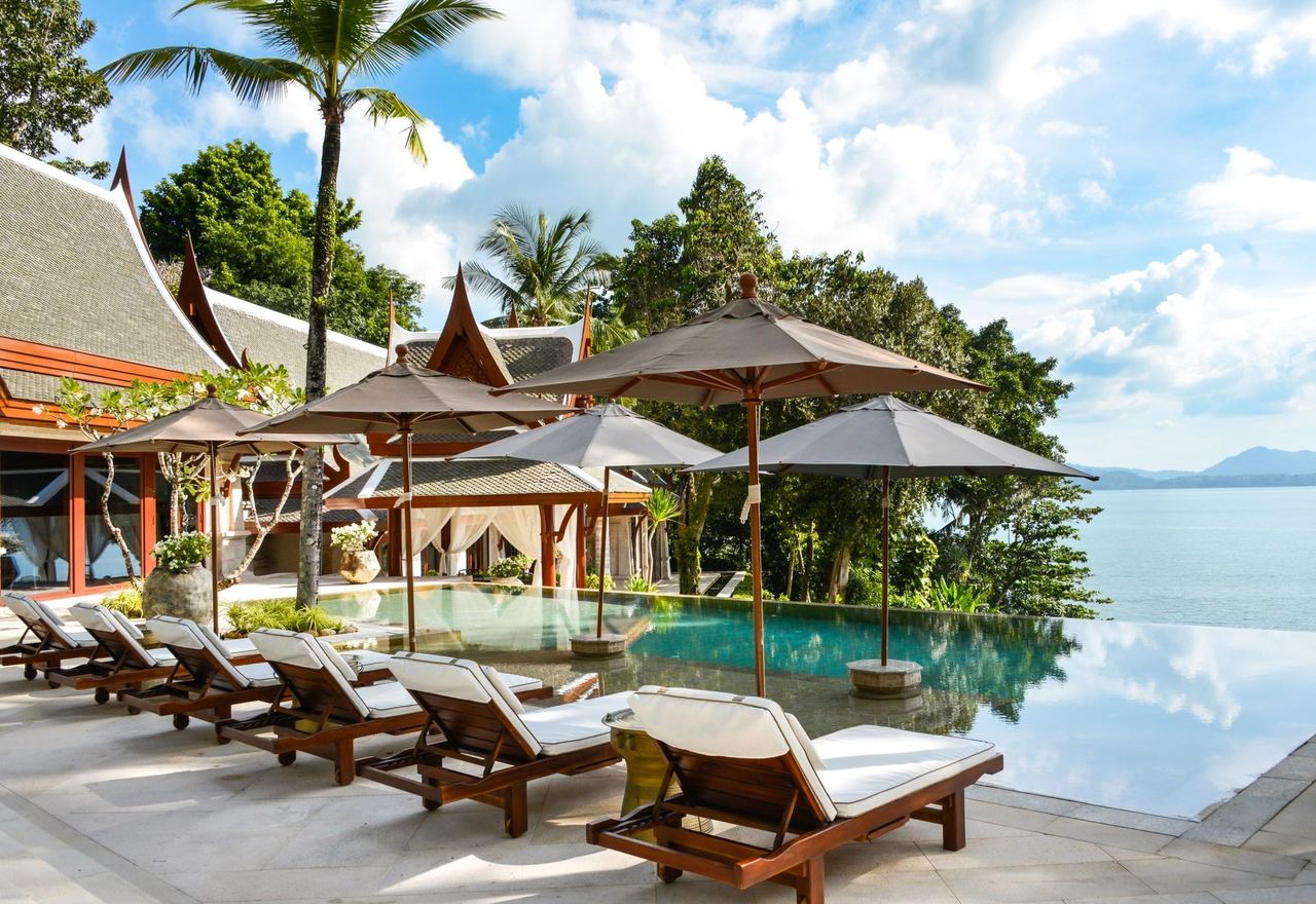 Loungers by an infinity pool beneath Thai rooflines at Trisara