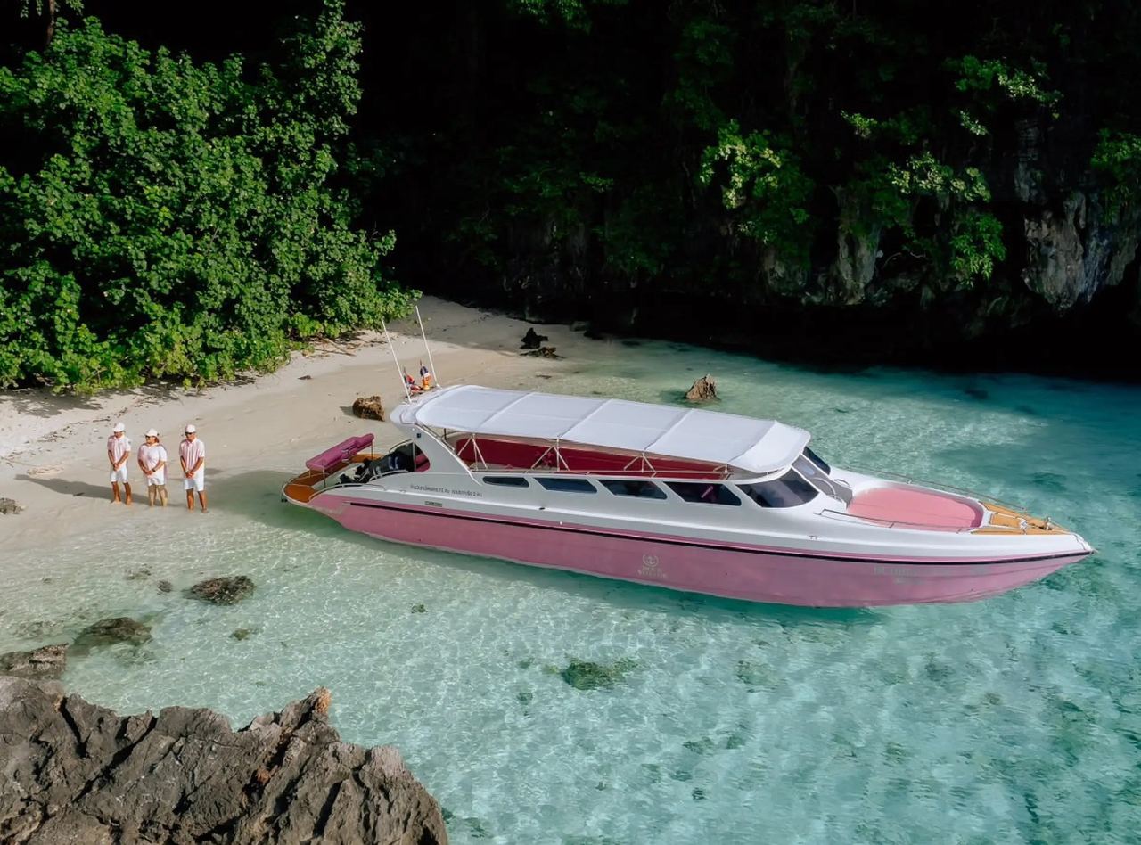 A pink Blue Voyage speedboat pulled up on a white-sand island beach with its crew