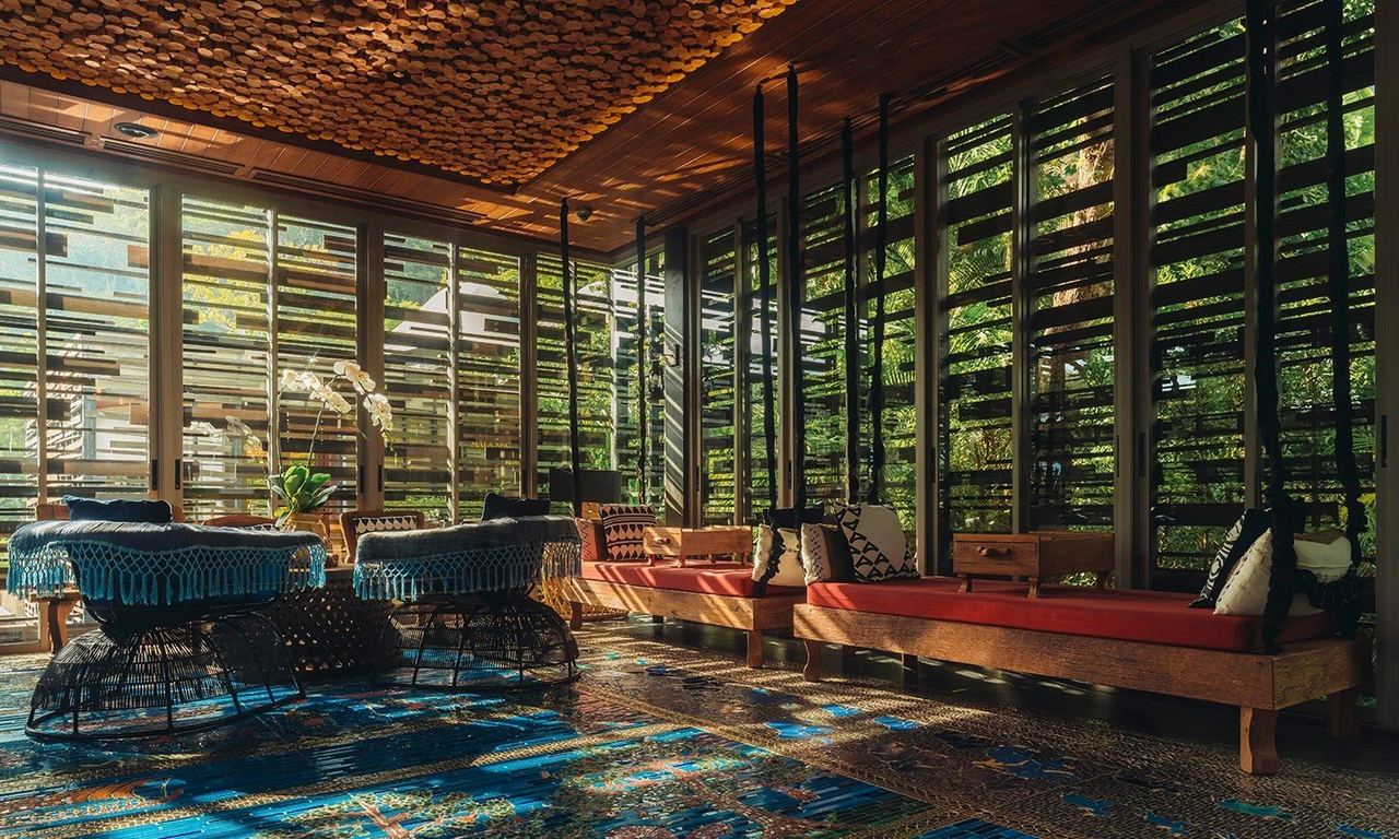 The lounge at Keemala, with louvred glass walls onto the rainforest, red daybeds and a patterned blue floor