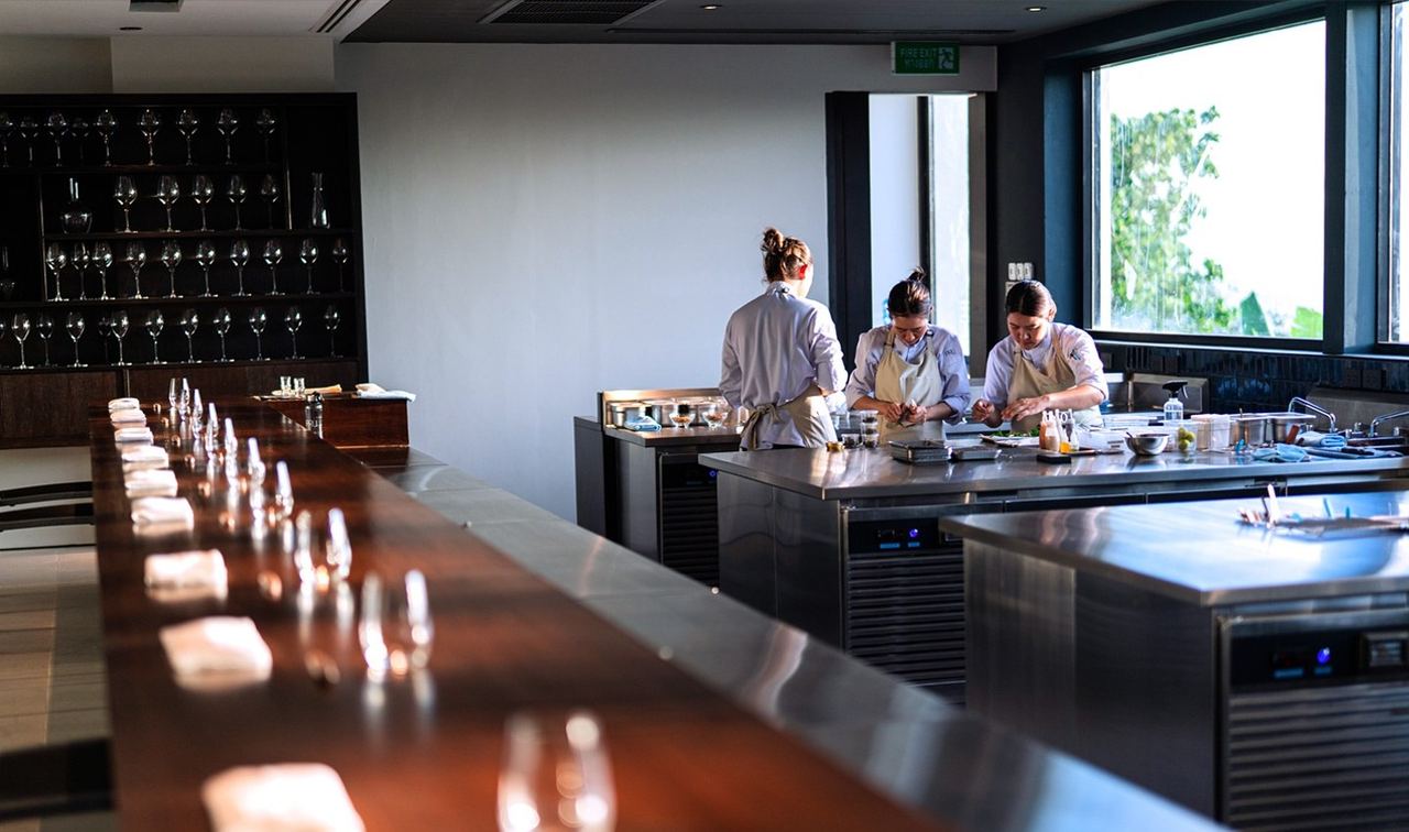 Cooks at work beyond the long wooden counter and wine glasses at PRU