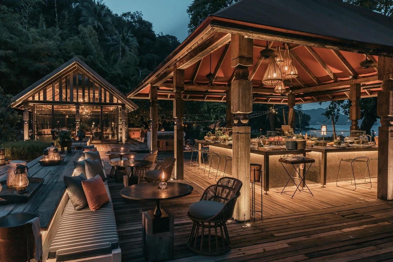 The timber pavilions and candlelit deck of Ta Khai at Rosewood Phuket at dusk